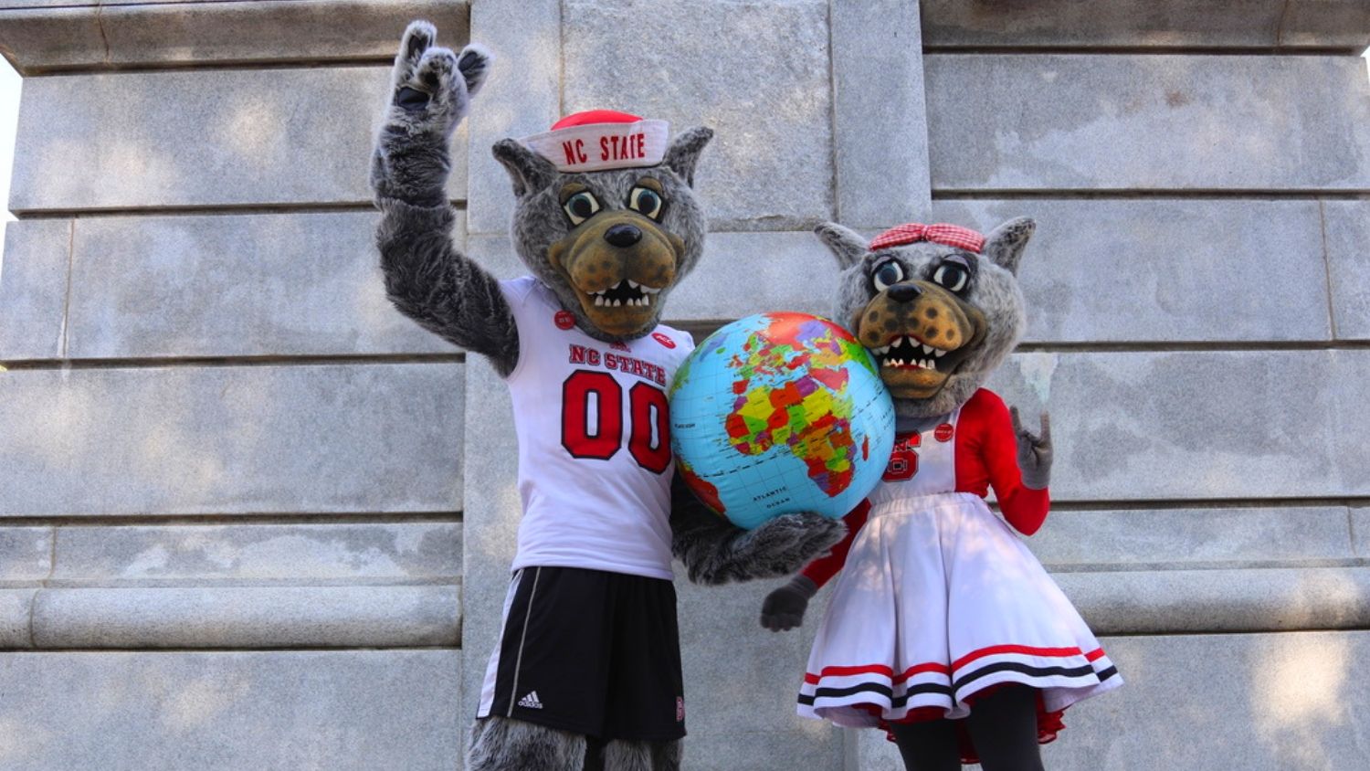 NC State's mascots, Mr and Mrs. Wuf, are holding a globe in front of the belltower.