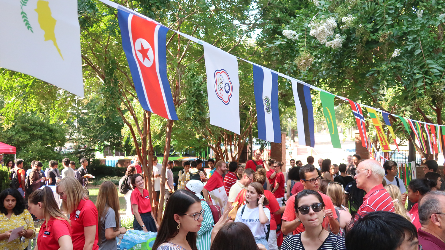A busy crowd of staff and students gathers oustide for the Global Welcome. The place is decorated with flags.