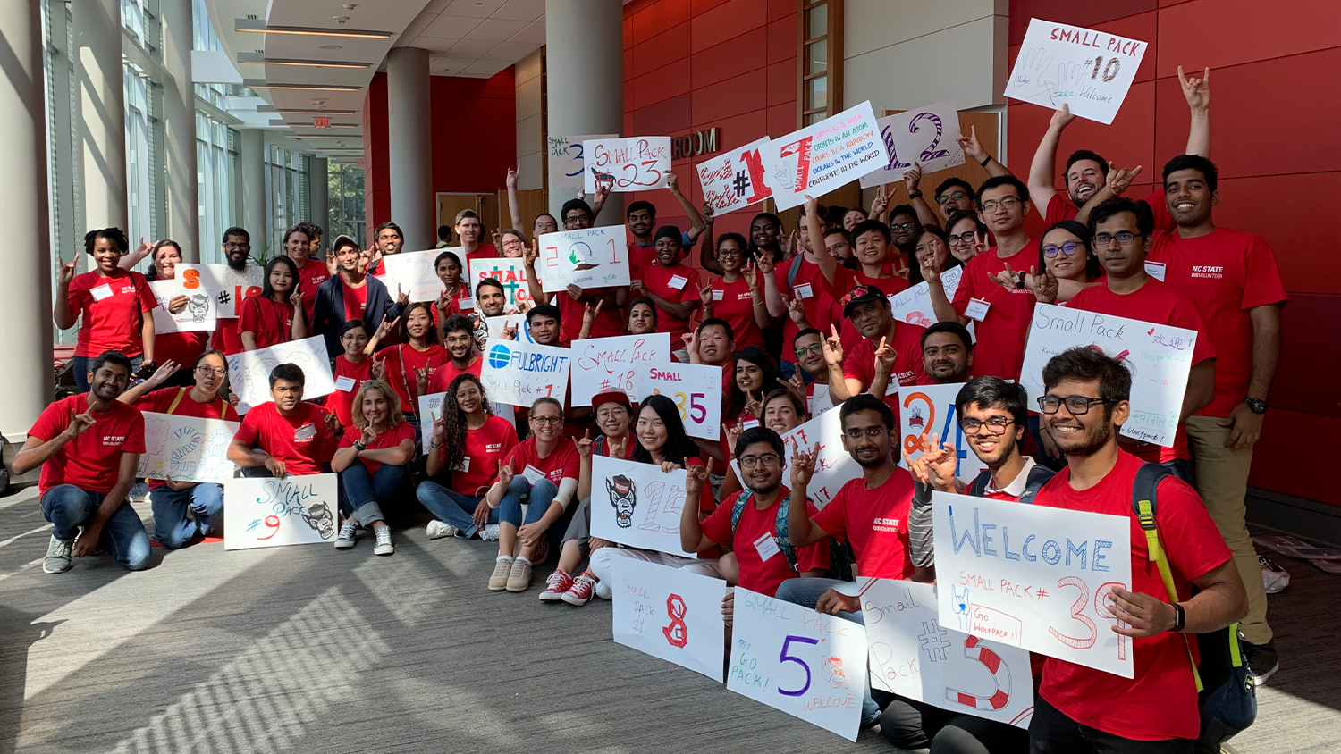 A group of international students volunteering as Small Pack Leaders are posing for a photo while holding up their group signs.