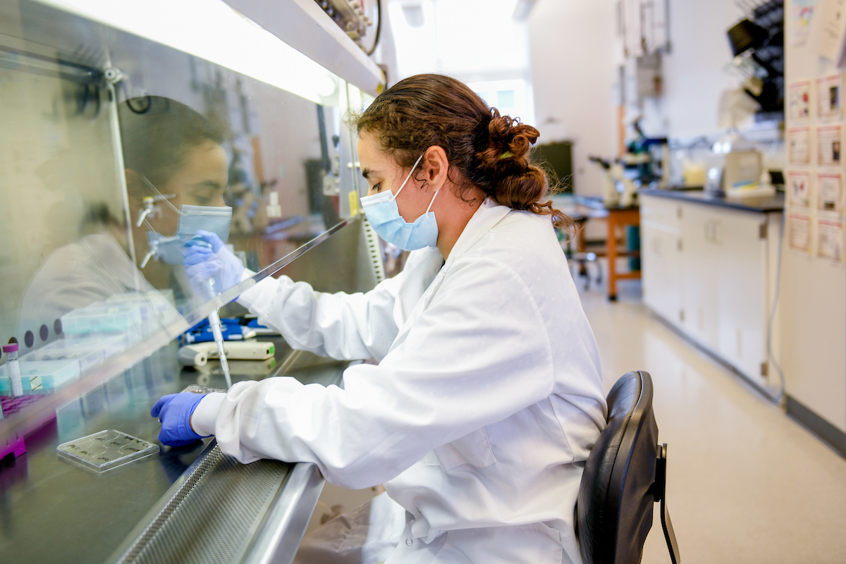 A woman with a mask on conducting biochem research in a lab. 