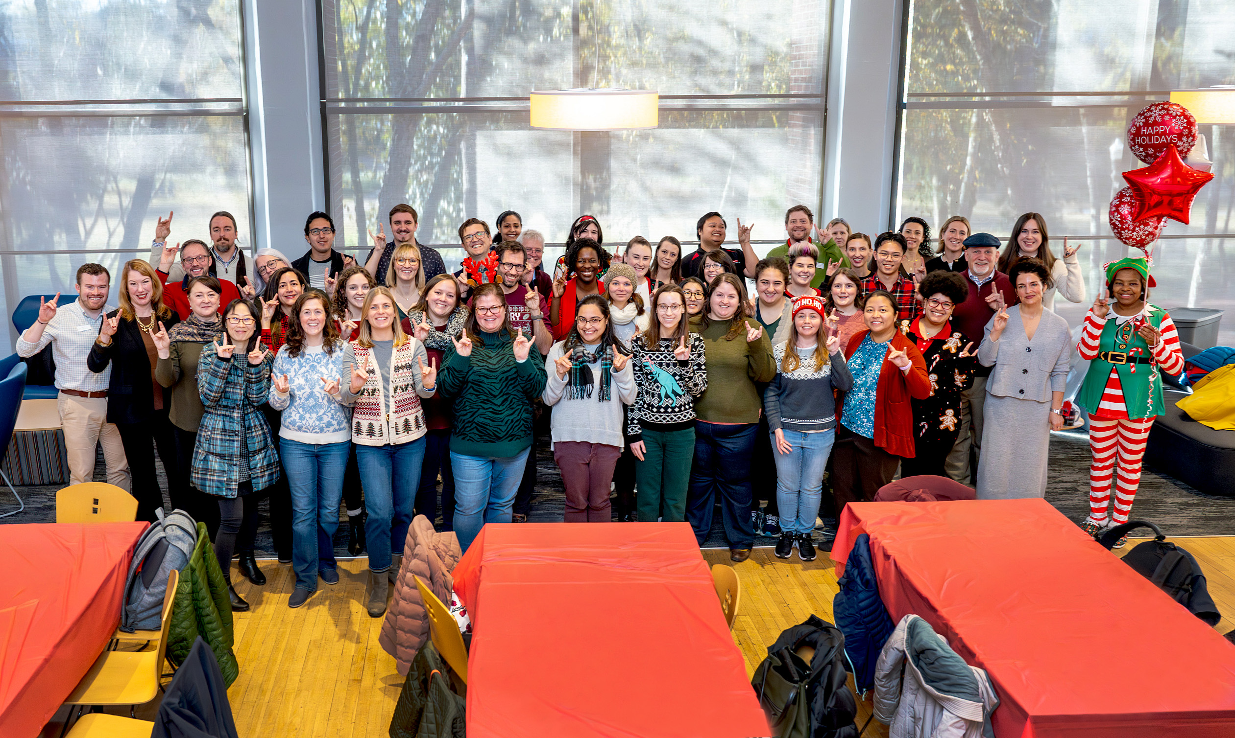 The entire staff of NC State Global pose in holiday attire at the Fall celebration while posing with Wolfies.