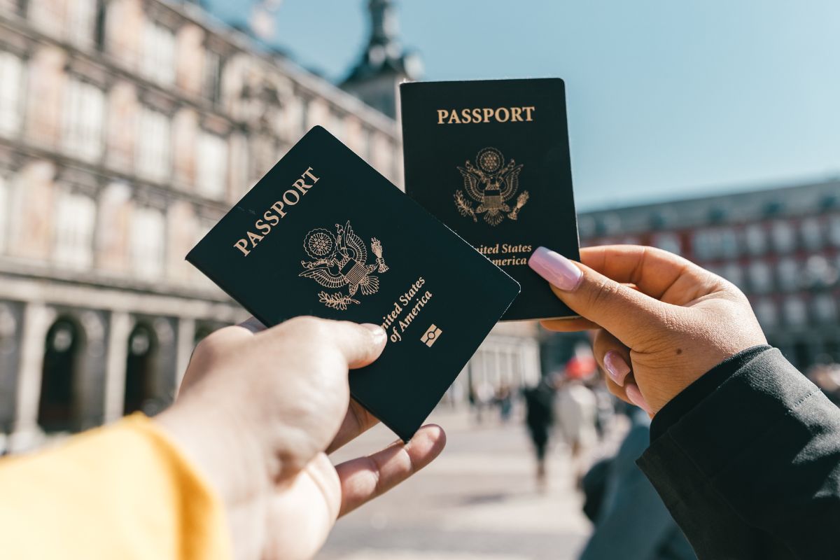 An image of two hands holding their passports in front of historic architecture abroad.
