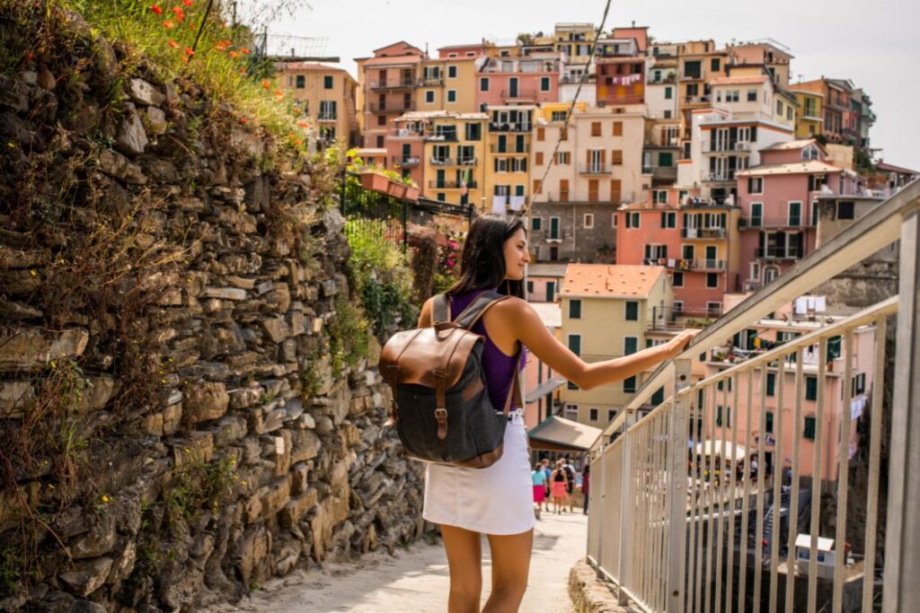 An image of a woman exploring a town in Italy, with a backdrop of colorful buildings and a mountainous landscape. 