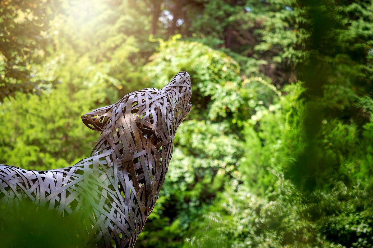 A sculptural wolf howling against a backdrop of trees. 