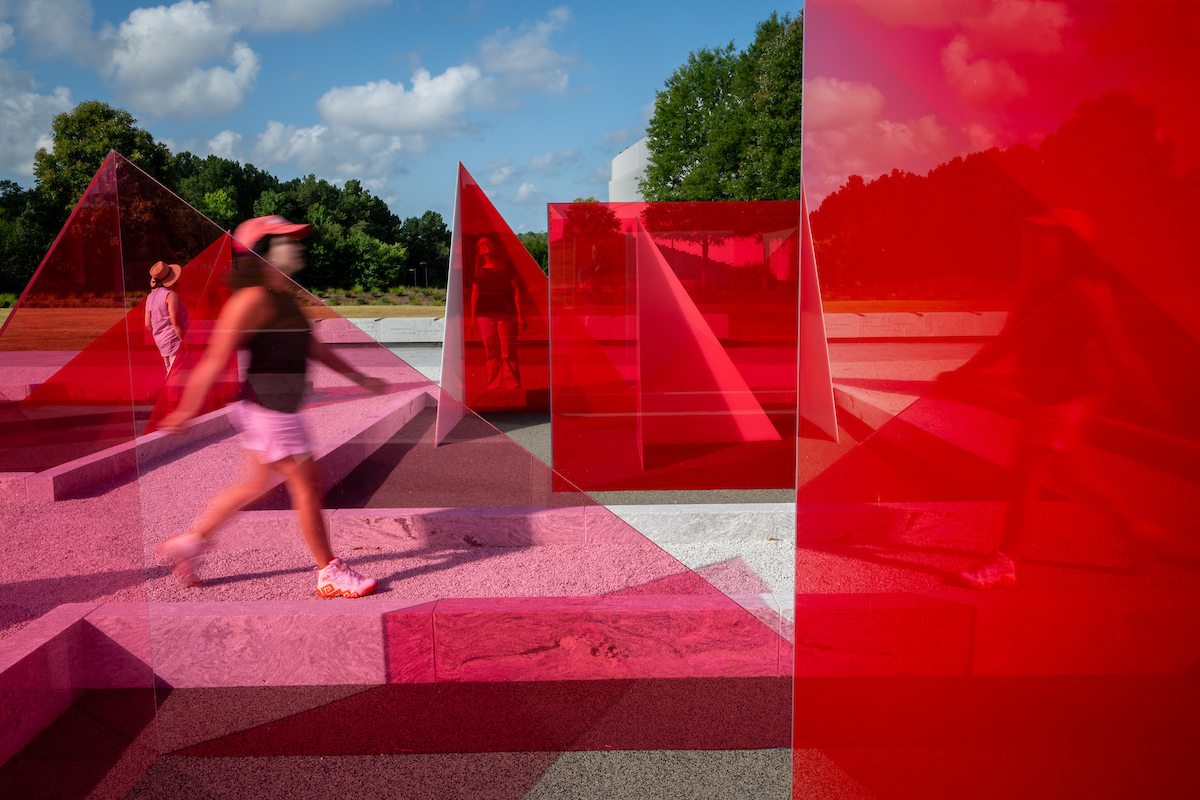 Red sculptural art at Centennial campus with people walking and observing the installation.