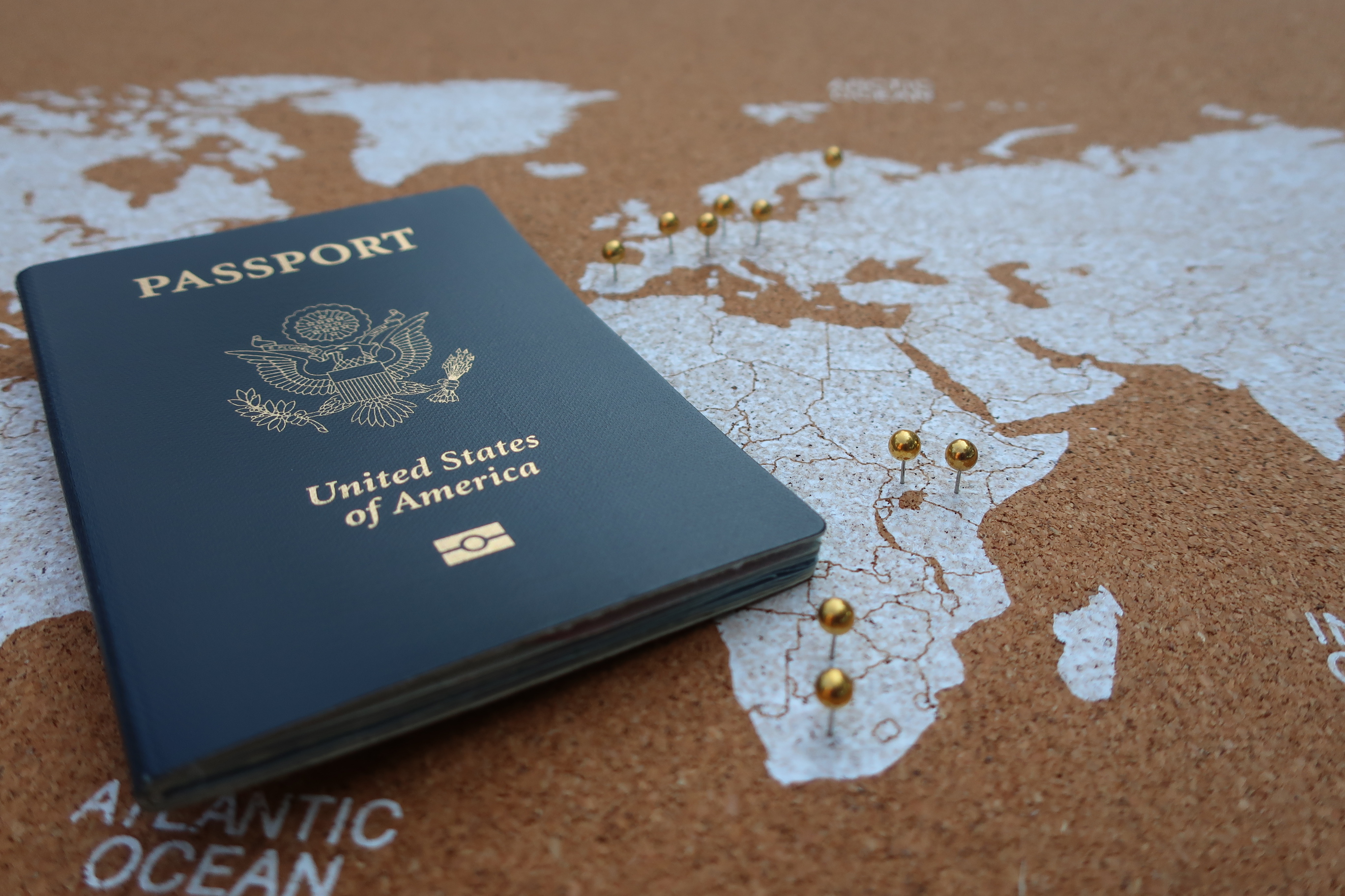 US passport laying on top of a world map that has pins it in indicating that the person has traveled there.