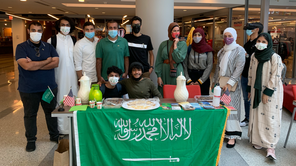 A group of students form Saudi Arabia pose in front of their booth (with a Saudi Arabia flag) in Talley Student Union.