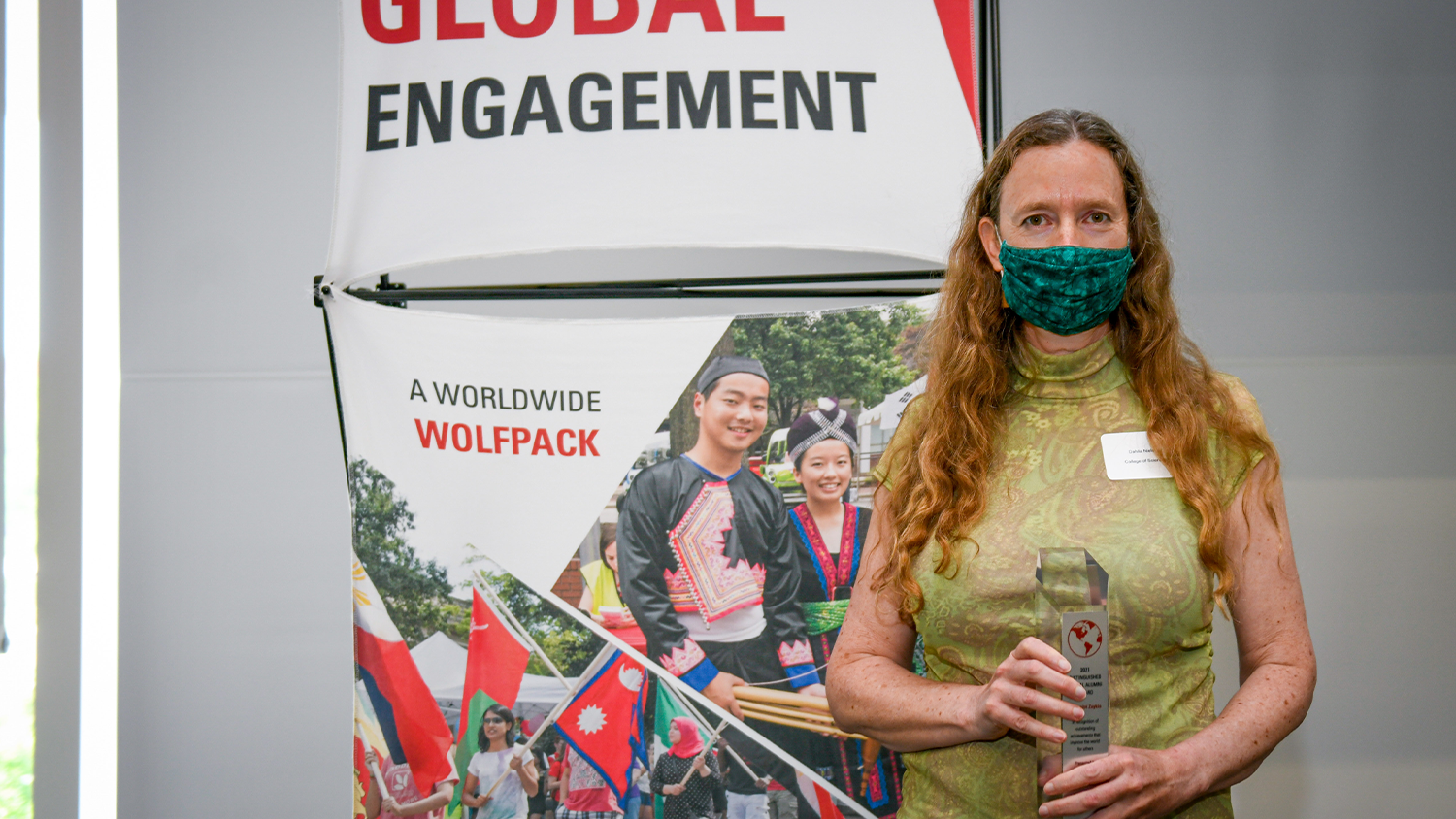A white woman holding up her award (Distinguished Global Alumni Award) in front of a NC State Global backdrop.
