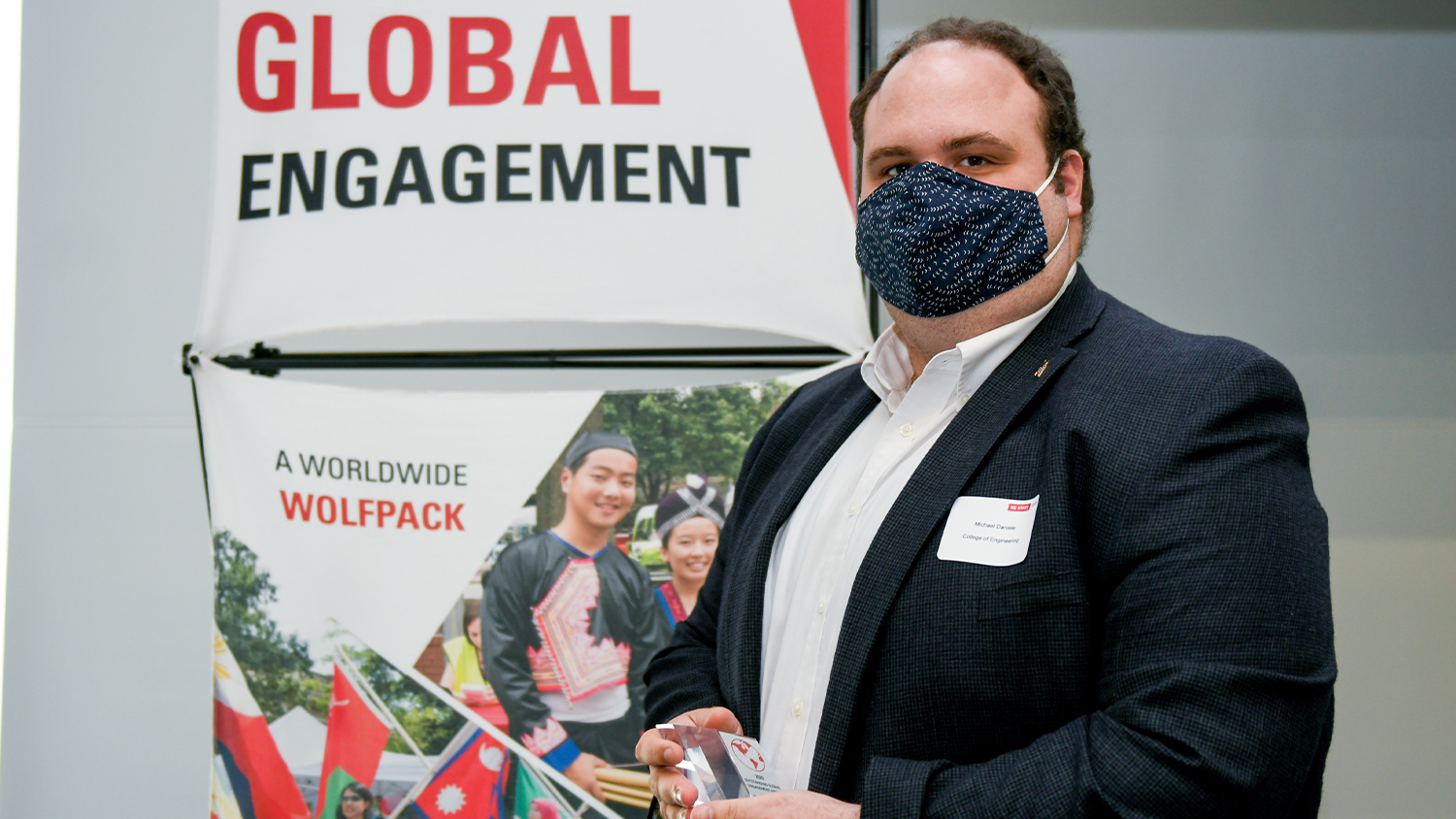 A white man holding up his award (Oustanding Global Engagement Award) in front of a NC State Global backdrop.