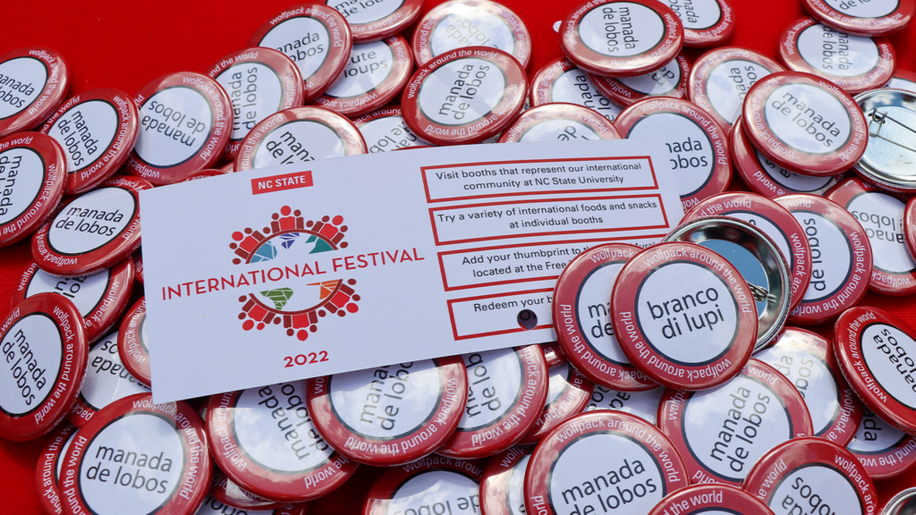 A "boarding pass" of the International Festival laying on buttons that say Wolfpack in different languages.