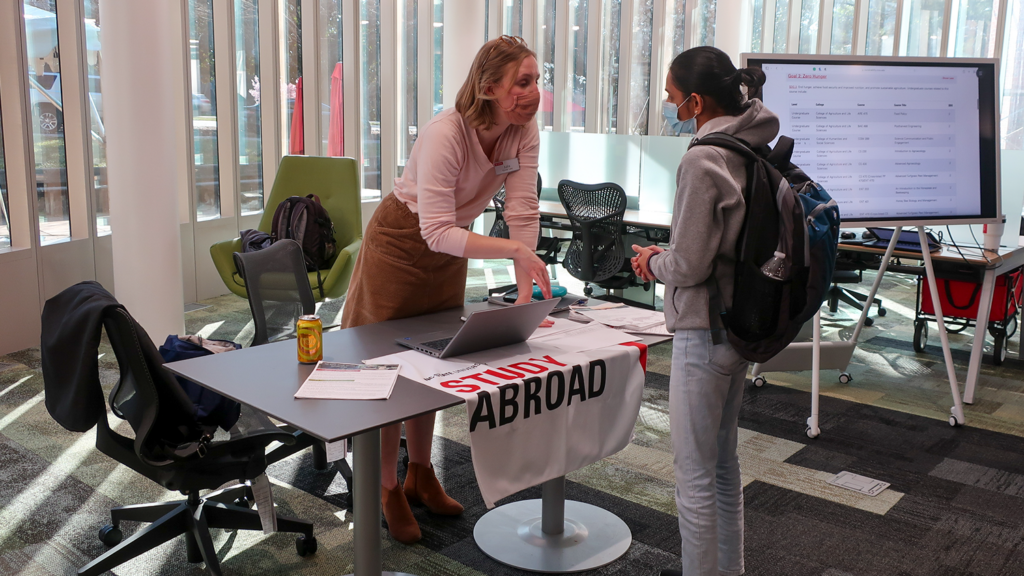 A blonde woman talking to a student about study abroad opportunities. 