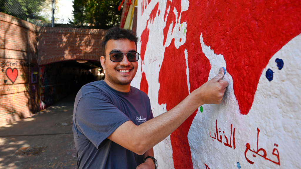 A student leaving his mark (thumb print dipped in paint) at the Wolfpack World mural in the free expression tunnel.